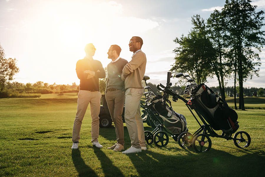 Medinah, IL Insurance - Three Business Associates Pause on the Golf Course at Sunset With Trees and Golf Bags Behind Them